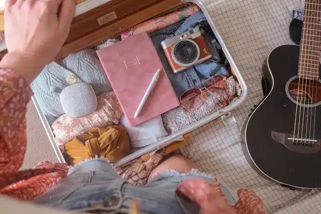 Checklist vacances avant de partir avec valise ouverte, vêtements, carnet, appareil photo et affaires de voyage