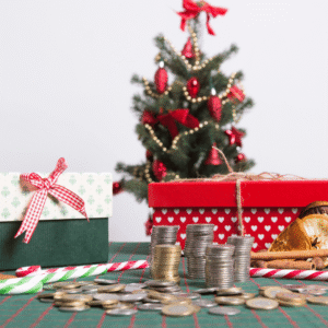 Piles de pièces de monnaie devant des boîtes cadeaux et un petit sapin de Noël décoré, pour illustrer le budget de Noël