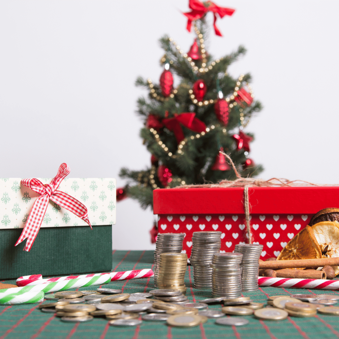 Piles de pièces de monnaie devant des boîtes cadeaux et un petit sapin de Noël décoré, pour illustrer le budget de Noël